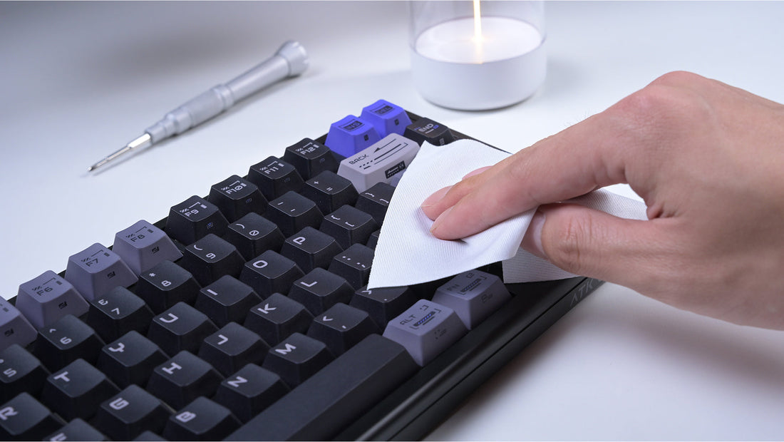 A person cleans a black mechanical keyboard with a white wipe.