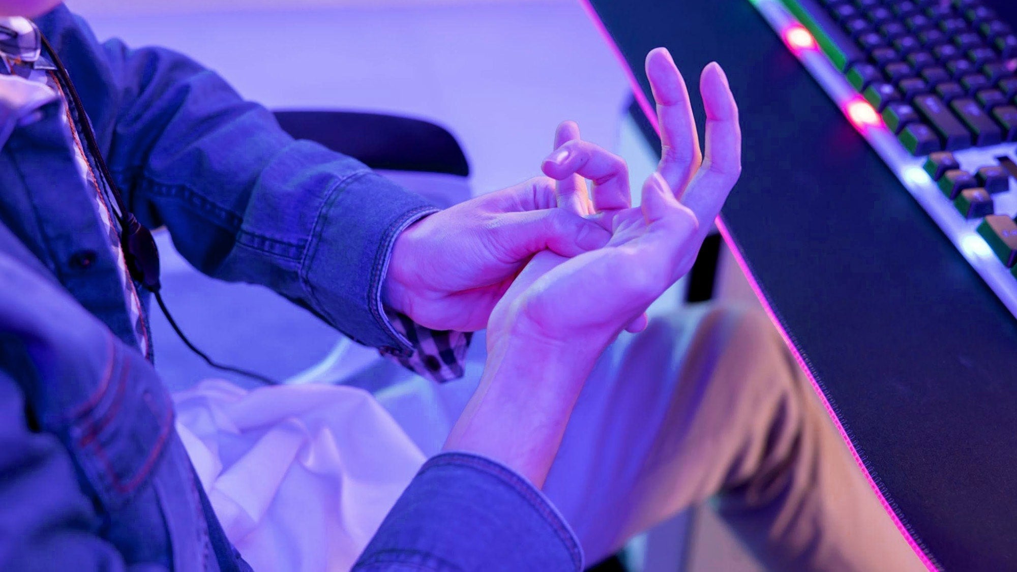 Why do my hands get tired while gaming: a gamer massaging a cramped palm to relieve strain near a PC keyboard setup.