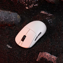 White ATK Dragonfly A9 lightweight wireless gaming mouse with matte finish on dark sand with rocks.