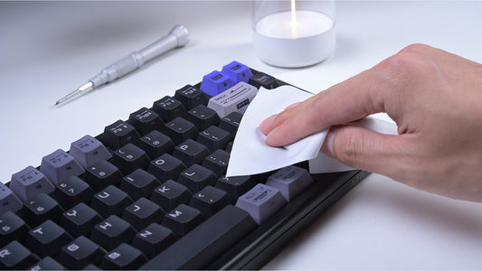 A person cleans a black mechanical keyboard with a white wipe.