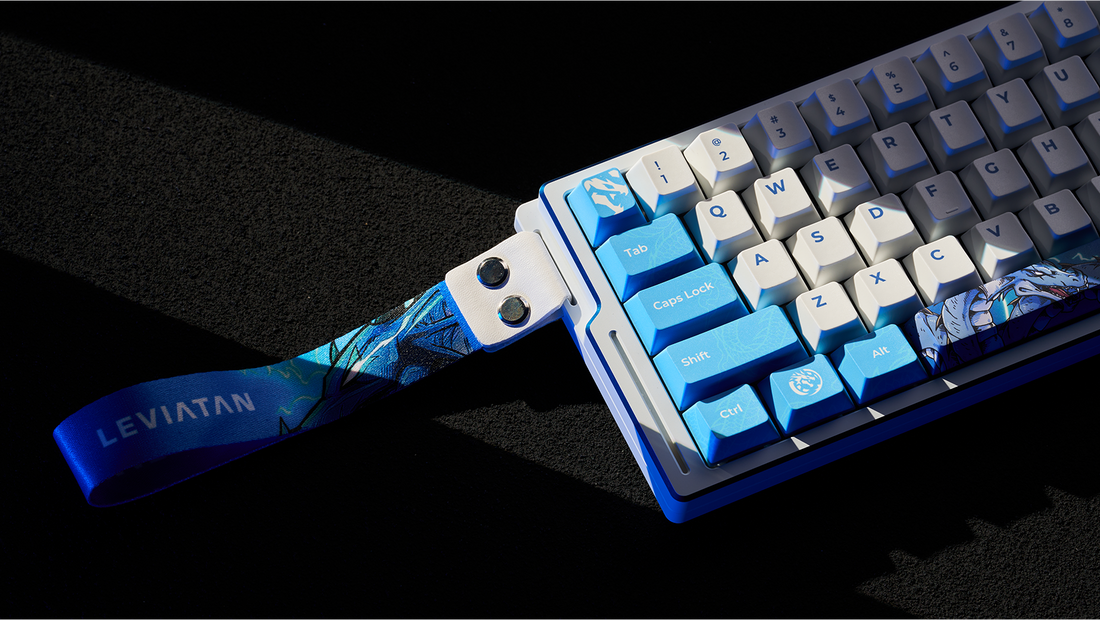 A close-up shot of a white and blue "LEVIATAN" themed mechanical keyboard, with a decorative strap attached, resting on a black textured surface.