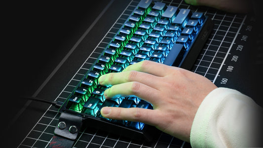 Hand typing on a compact RGB mechanical keyboard with blue and green backlighting
