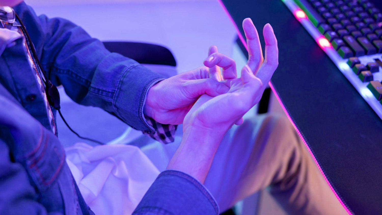 Why do my hands get tired while gaming: a gamer massaging a cramped palm to relieve strain near a PC keyboard setup.