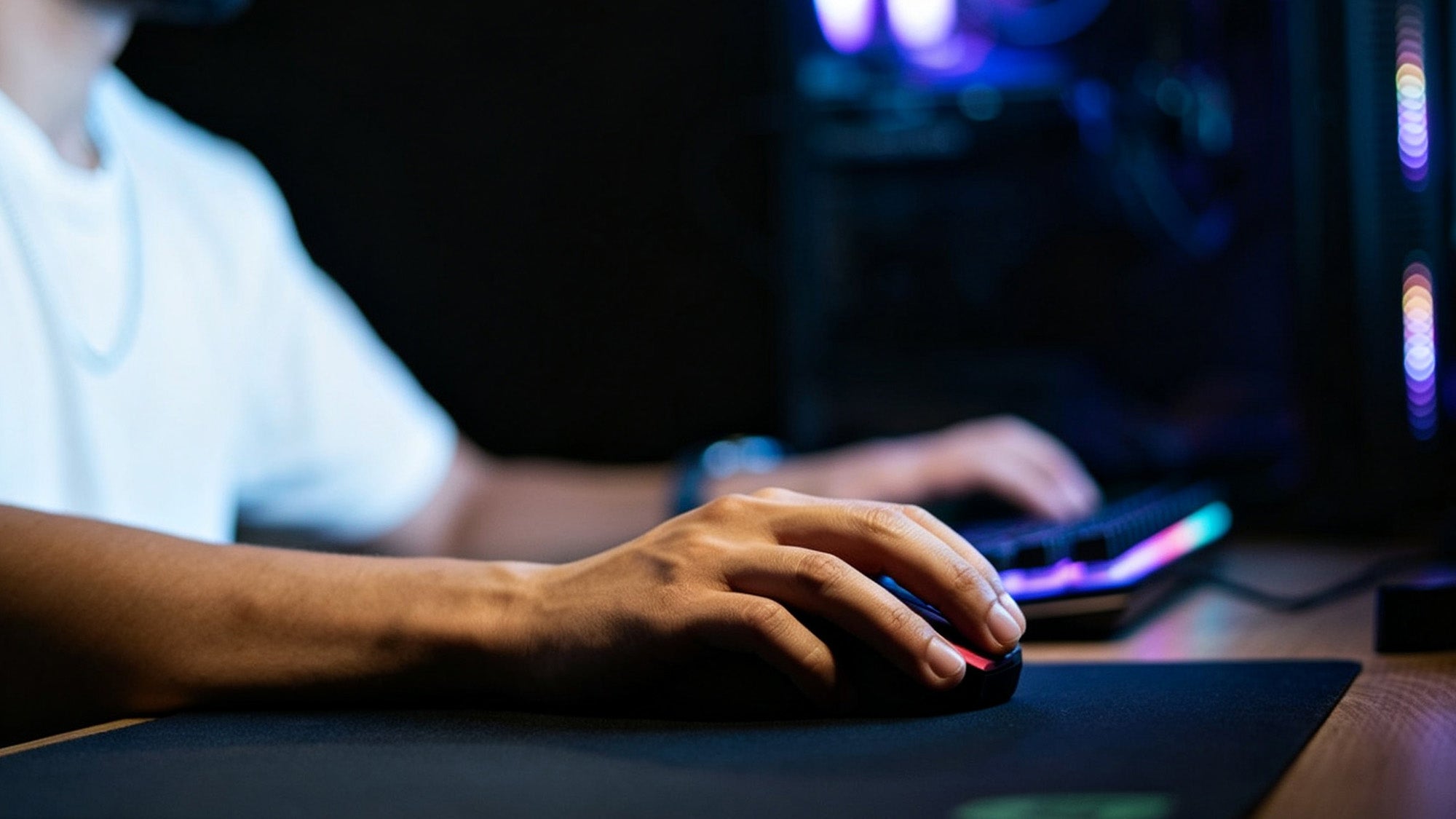 Gamer using a wireless gaming mouse on a mouse pad in a dark RGB-lit setup