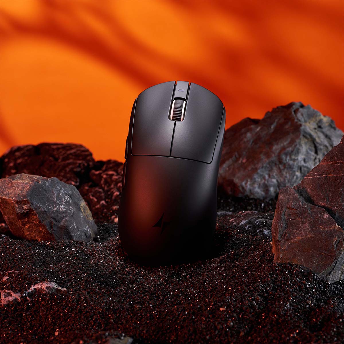ATK Dragonfly A9 black gaming mouse on sand with rocks. Textured scroll wheel and ATK logo visible.