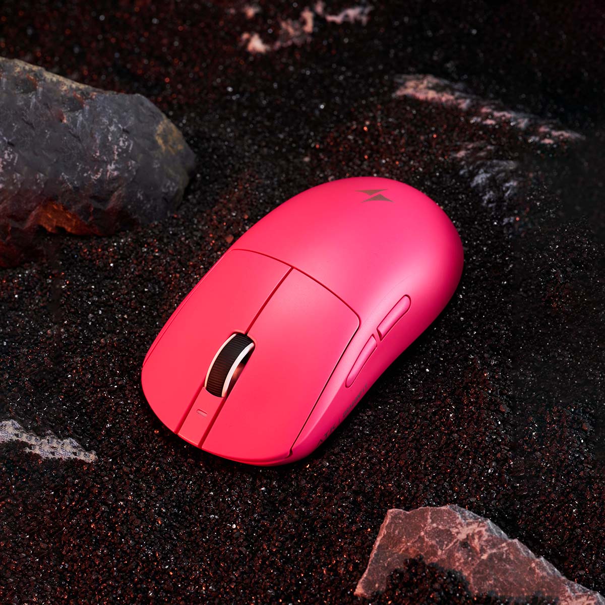 Pink ATK Dragonfly A9 ergonomic gaming mouse with a black scroll wheel, placed on black sand with rocks.